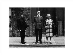 Three people stand on street facing the camera: 1961