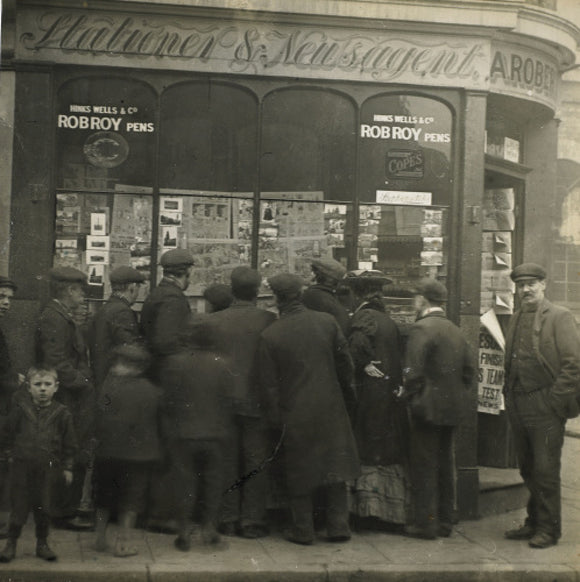 A crowd gathered around an East End newsagents window display: c.1900