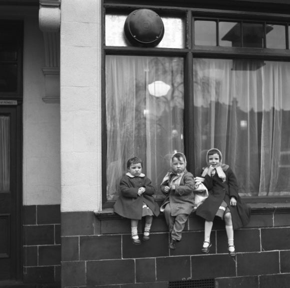 Three children perched on the windowsill of a pub. c.1955
